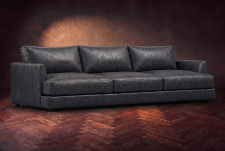 The Serena sofa in Aged Slate distressed full leather on a dark walnut herringbone floor, three-quarter view. Shown in Aged Slate.