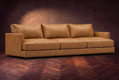 The Serena sofa in Antiqued Caramel distressed full leather on a dark walnut herringbone floor, three-quarter view. Shown in Antiqued Caramel.