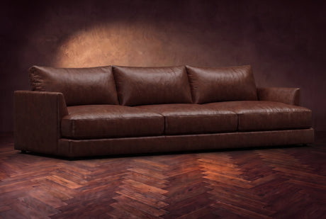 The Serena sofa in Burnished Chestnut distressed full leather on a dark walnut herringbone floor, three-quarter view. Shown in Burnished Chestnut.