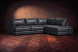 The Serena sectional in Aged Slate distressed full leather on a walnut herringbone floor against a dark plaster wall, three-quarter view. Shown in Aged Slate, Right bumper.