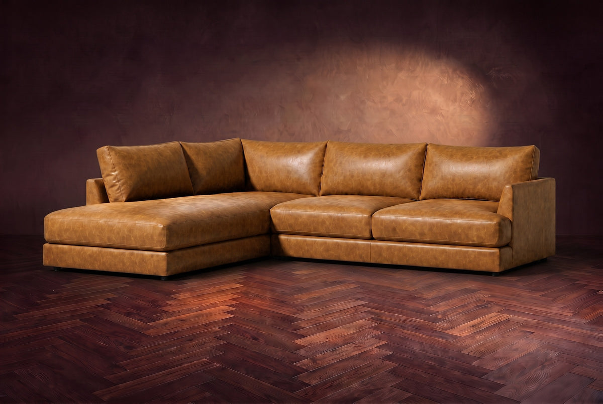 The Serena sectional in Antiqued Caramel distressed full leather on a walnut herringbone floor against a dark plaster wall, three-quarter view. Shown in Antiqued Caramel, Left bumper.