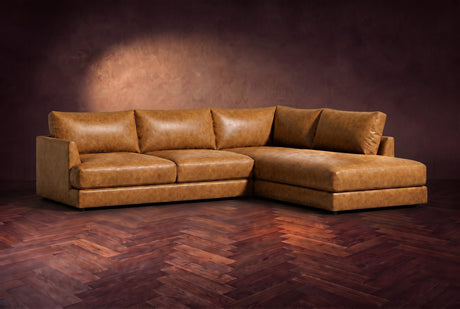 The Serena sectional in Antiqued Caramel distressed full leather on a walnut herringbone floor against a dark plaster wall, three-quarter view. Shown in Antiqued Caramel, Right bumper.