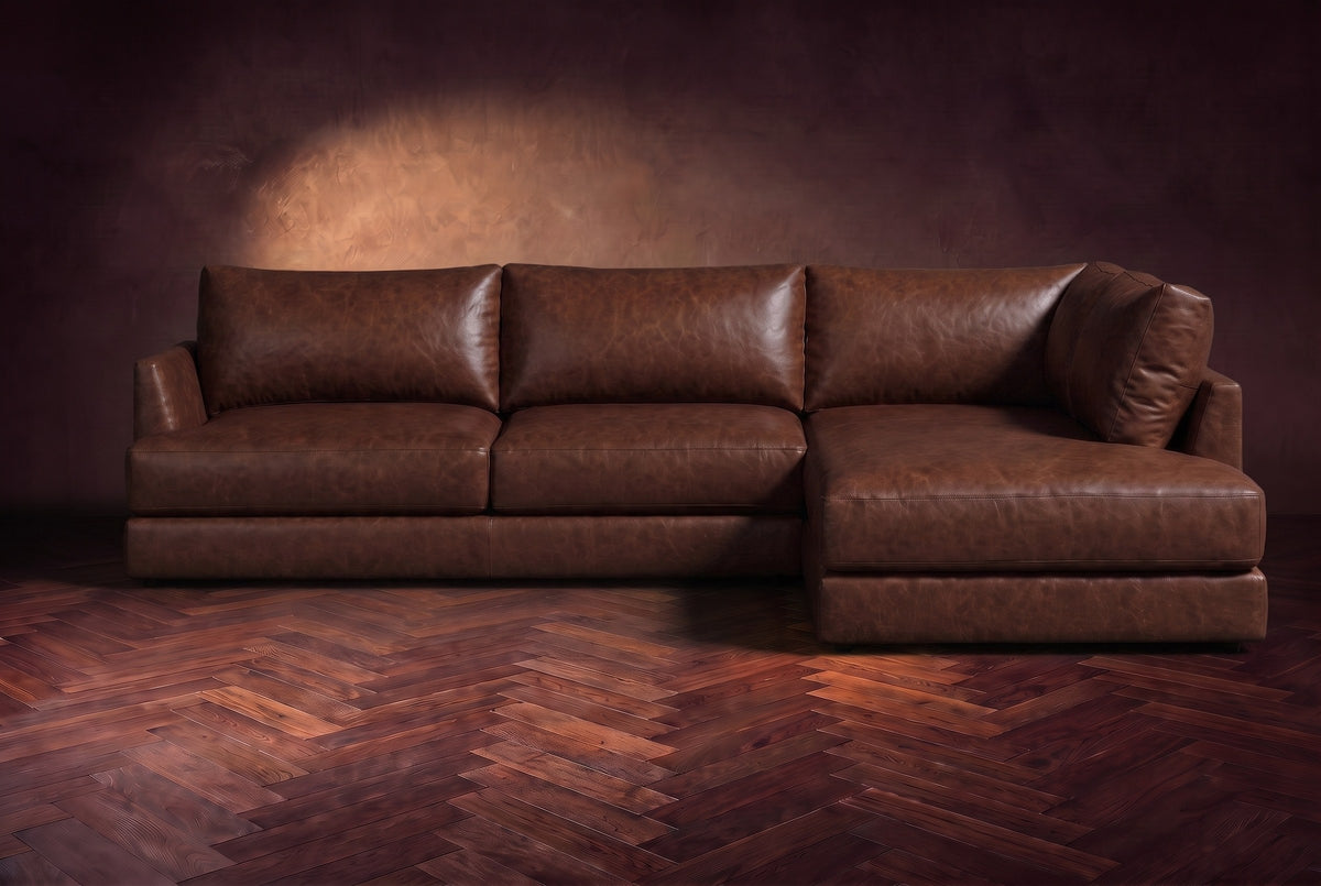 The Serena sectional in Burnished Chestnut distressed full leather on a walnut herringbone floor against a dark plaster wall, seen from the front. Shown in Burnished Chestnut, Right bumper.