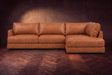 The Serena sectional in Tuscan Cognac distressed full leather on a walnut herringbone floor against a dark plaster wall, seen from the front. Shown in Tuscan Cognac, Right bumper.