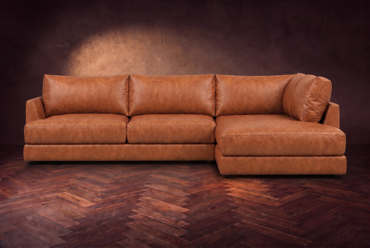 The Serena sectional in Tuscan Cognac distressed full leather on a walnut herringbone floor against a dark plaster wall, seen from the front. Shown in Tuscan Cognac, Right bumper.
