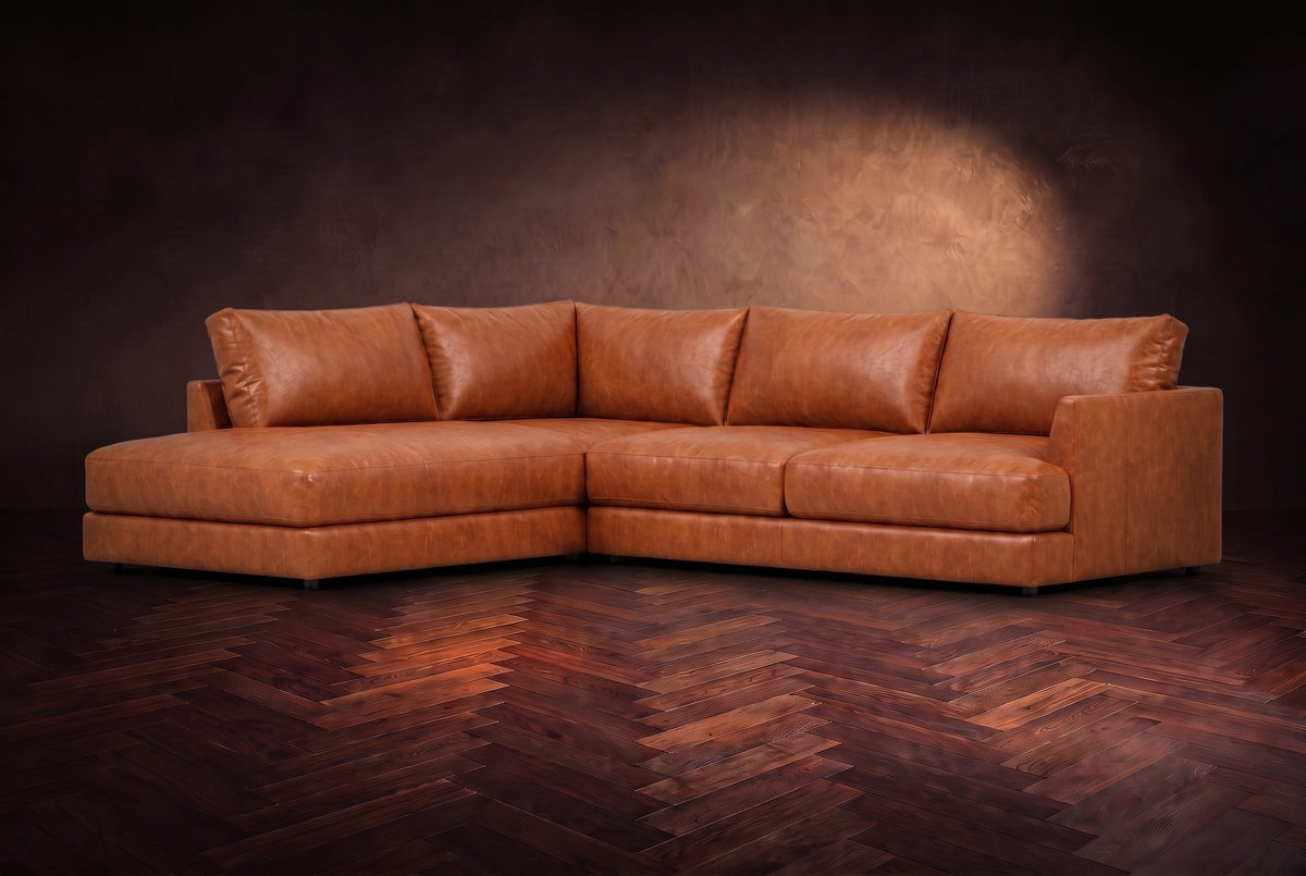 The Serena sectional in Tuscan Cognac distressed full leather on a walnut herringbone floor against a dark plaster wall, three-quarter view. Shown in Tuscan Cognac, Left bumper.