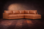 The Serena sectional in Tuscan Cognac distressed full leather on a walnut herringbone floor against a dark plaster wall, three-quarter view. Shown in Tuscan Cognac, Right bumper.