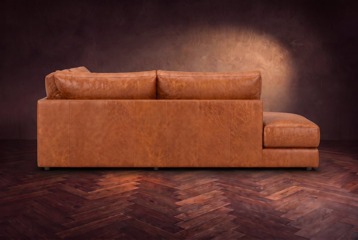The Serena sectional in Tuscan Cognac distressed full leather on a walnut herringbone floor against a dark plaster wall, seen from the chaise side. Shown in Tuscan Cognac, Left bumper.