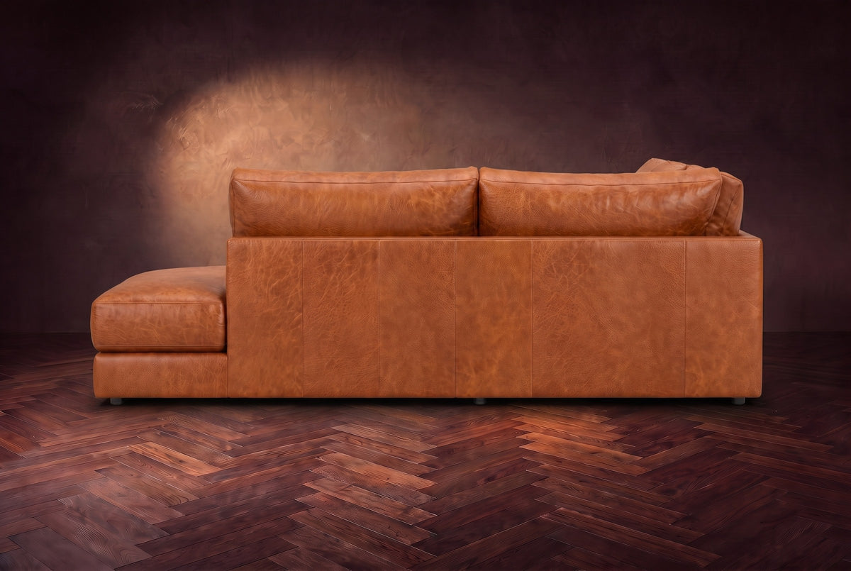 The Serena sectional in Tuscan Cognac distressed full leather on a walnut herringbone floor against a dark plaster wall, seen from the chaise side. Shown in Tuscan Cognac, Right bumper.