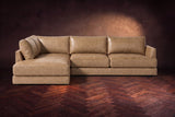 The Serena sectional in Washed Sand distressed full leather on a walnut herringbone floor against a dark plaster wall, seen from the front. Shown in Washed Sand, Left bumper.