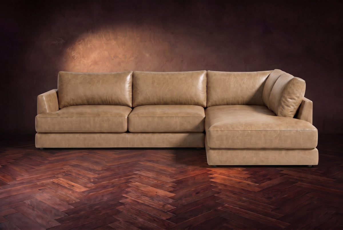 The Serena sectional in Washed Sand distressed full leather on a walnut herringbone floor against a dark plaster wall, seen from the front. Shown in Washed Sand, Right bumper.