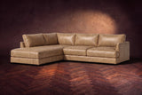 The Serena sectional in Washed Sand distressed full leather on a walnut herringbone floor against a dark plaster wall, three-quarter view. Shown in Washed Sand, Left bumper.