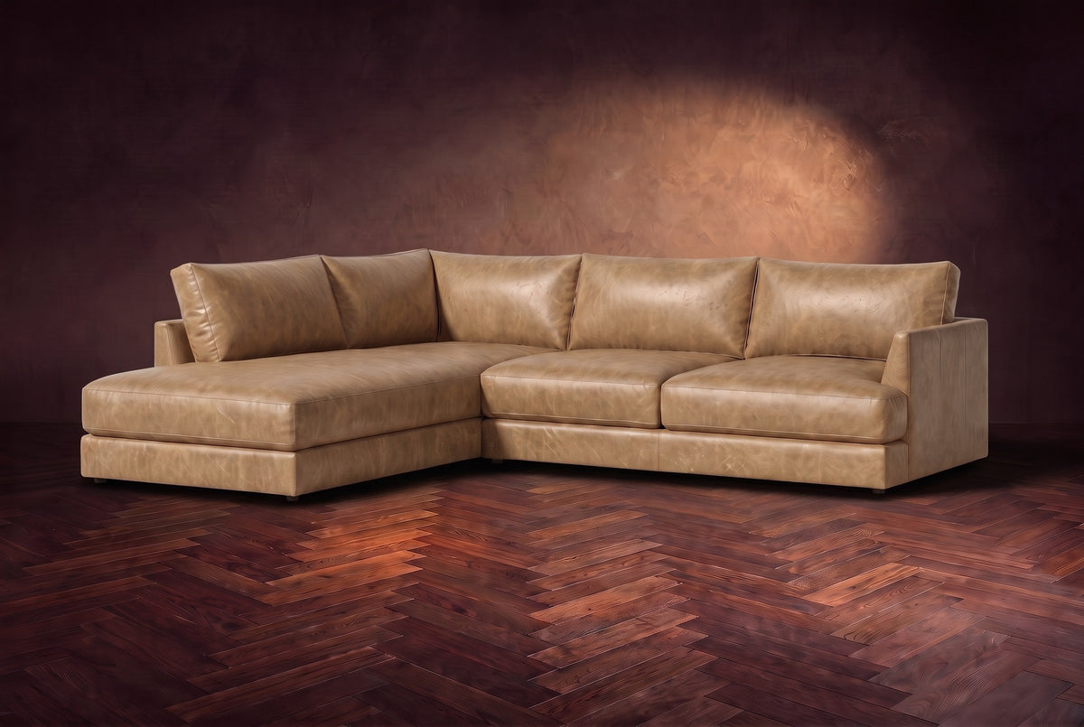 The Serena sectional in Washed Sand distressed full leather on a walnut herringbone floor against a dark plaster wall, three-quarter view. Shown in Washed Sand, Left bumper.