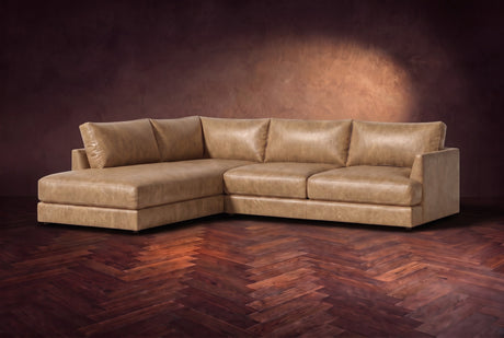 The Serena sectional in Washed Sand distressed full leather on a walnut herringbone floor against a dark plaster wall, three-quarter view. Shown in Washed Sand, Left bumper.