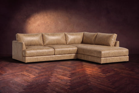The Serena sectional in Washed Sand distressed full leather on a walnut herringbone floor against a dark plaster wall, three-quarter view. Shown in Washed Sand, Right bumper.