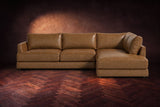 The Serena sectional in Weathered Saddle distressed full leather on a walnut herringbone floor against a dark plaster wall, seen from the front. Shown in Weathered Saddle, Right bumper.