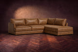 The Serena sectional in Weathered Saddle distressed full leather on a walnut herringbone floor against a dark plaster wall, three-quarter view. Shown in Weathered Saddle, Right bumper.