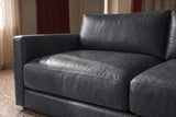 Close-up of the Serena corner sectional's slim track arm running the full depth of the seat, beside sheer linen curtains on a terrazzo floor. Shown in Aged Slate.
