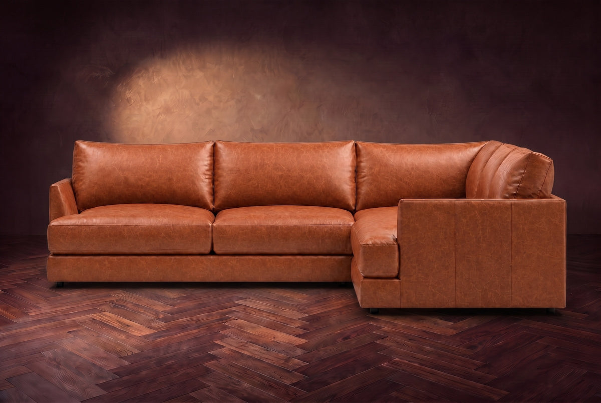 Serena corner sectional in Tuscan Cognac on a walnut herringbone floor, seen from the front with the near side on the right.
