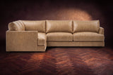 Serena corner sectional in Washed Sand on a walnut herringbone floor, seen from the front with the near side on the left.
