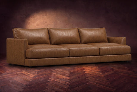 The Serena sofa in Weathered Saddle distressed full leather on a dark walnut herringbone floor, three-quarter view. Shown in Weathered Saddle.