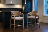 Two Sermoneta counter stools in Natural Ash pulled out from a stone-topped island in a dark green Toronto kitchen at dusk