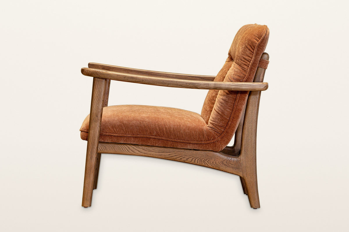 Servigliano accent chair in Rust, side view on a warm white studio backdrop: the long flat arm