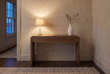 Sestri console table in walnut in a limewashed Halifax hallway at dusk, a brass lamp lit and dried branches in a white vase