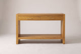 Sibari console table in Natural, straight front view: two drawers with gold-tone pulls, slab sides and a low shelf