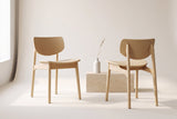 Two Simone dining chairs in natural oak, front and back views, beside a pale oak block with a white vase