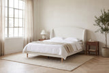 Sirmione boucle wingback bed made up with white linen in a loft bedroom with tall factory windows and an olive tree