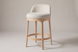Sirolo round counter stool in brushed natural wood with a beige seat, three-quarter view on a warm light-grey studio backdrop