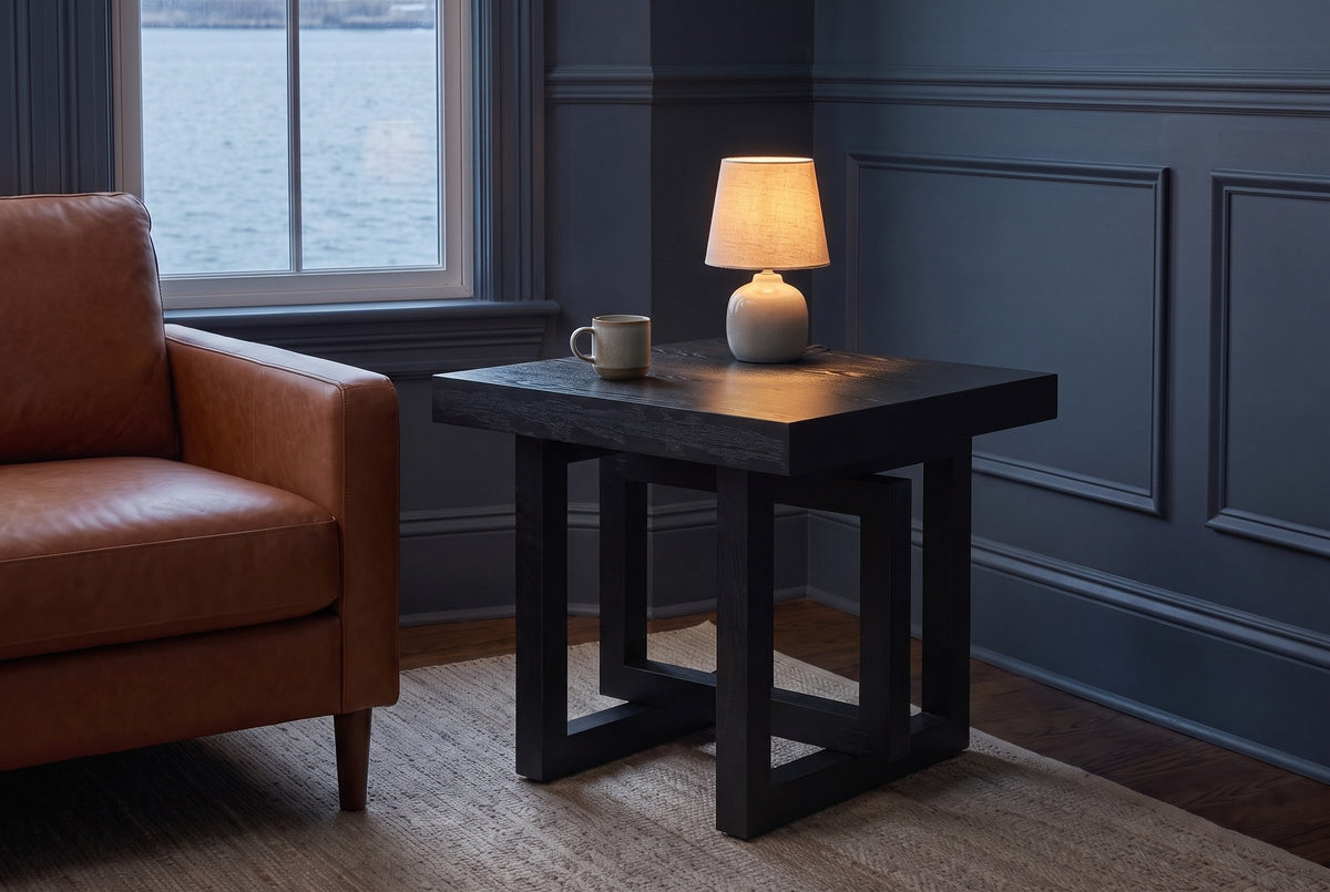 Soave side table in black beside a cognac leather armchair in a blue-grey Halifax front room at dusk, a small lamp lit on top