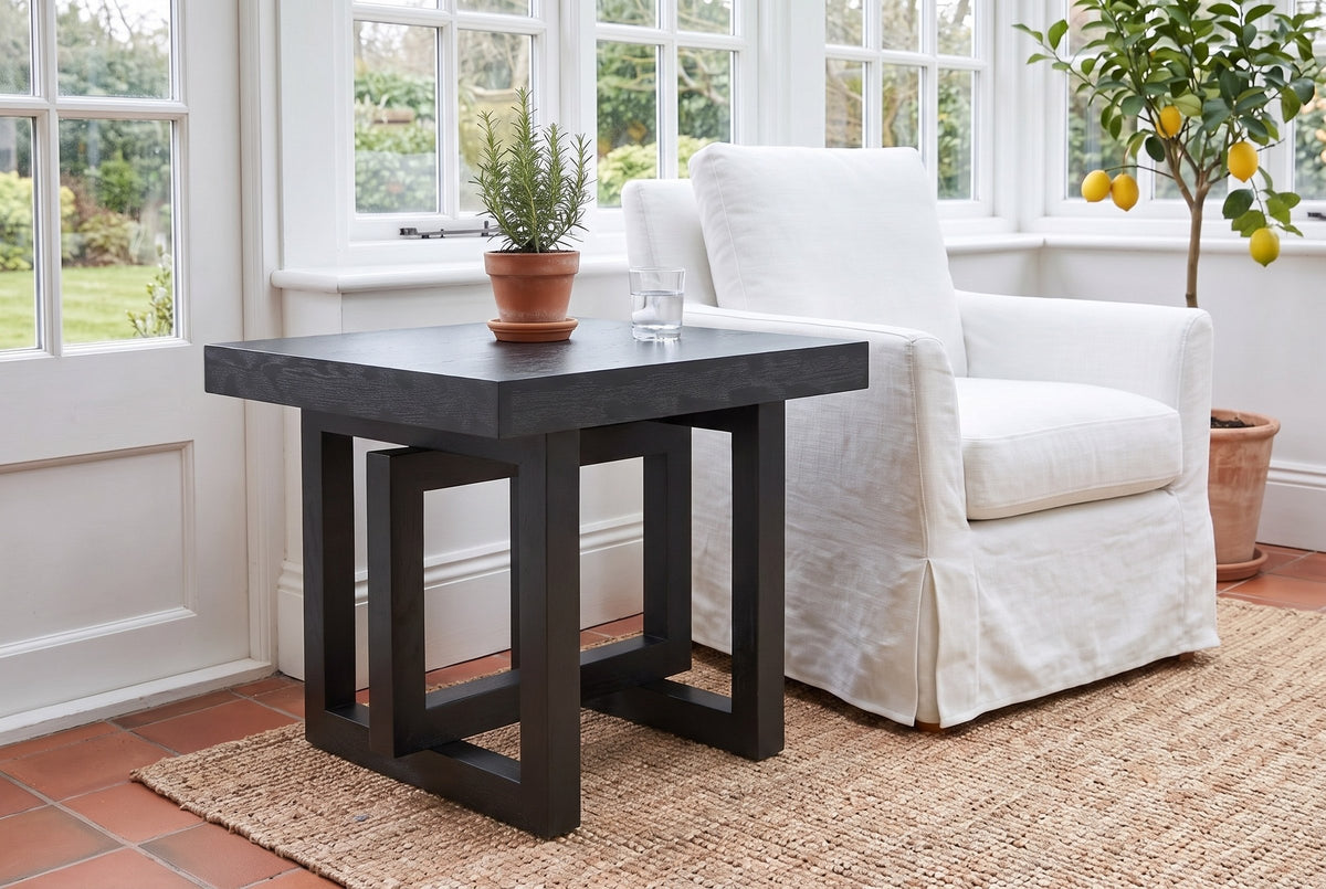 Soave side table in black beside a white slipcovered armchair in a Victoria garden room, rosemary and a glass of water on top
