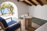 Sorano side table seen from above beside an indigo armchair in a whitewashed island house on Sifnos, with slate floors