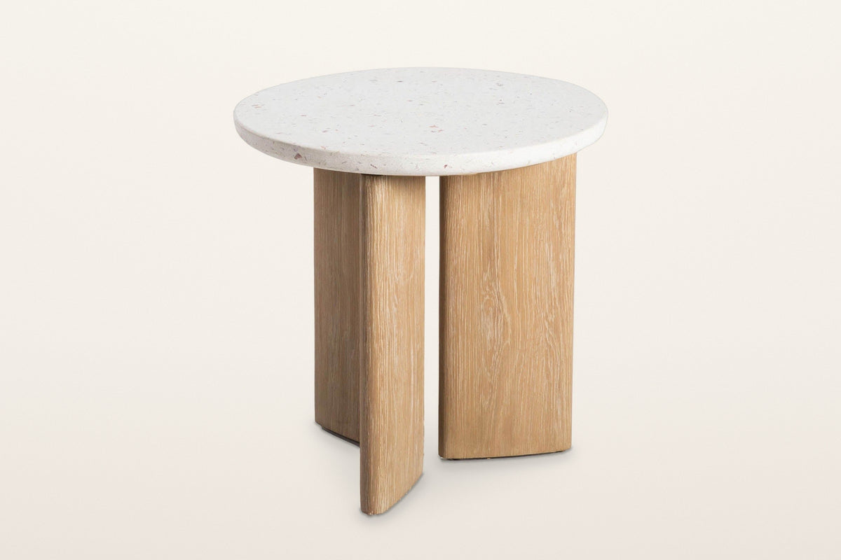 Sorano side table, three-quarter view from above on a warm white studio backdrop: a round seashell terrazzo top on three oak