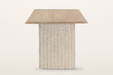 Staffolo dining table in Natural, end view on a warm white studio backdrop: the top overhangs a wide reeded marble pedestal