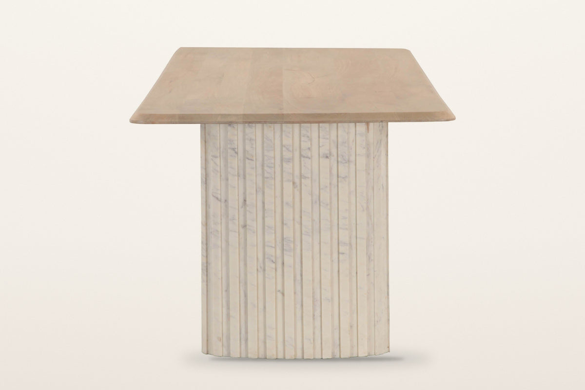 Staffolo dining table in Natural, end view on a warm white studio backdrop: the top overhangs a wide reeded marble pedestal