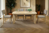 Sylvan dining table with grey upholstered chairs in a warm, plant-filled dining room