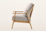 Tagliacozzo accent chair from the side on a warm white studio backdrop: the arm sweeping up into the back post