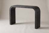 Tarvisio waterfall console table in black, three-quarter view on a warm grey studio backdrop