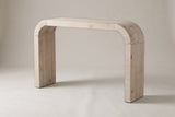 Tarvisio waterfall console table in the natural finish, three-quarter view on a warm grey studio backdrop