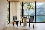Two Teggiano dining chairs in Black at a round limestone pedestal table in a Britannia Beach house, with a limestone wall