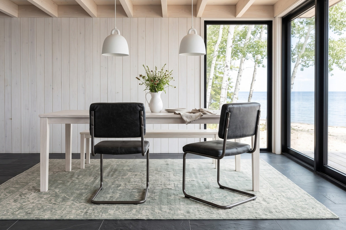 Two Tenno dining chairs in Black seen from behind at a whitewashed ash table in a Gimli lake house, glass to birches
