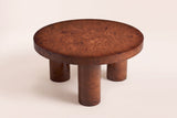 Teramo round coffee table in a walnut burl veneer finish, three-quarter view on a warm cream studio backdrop: a thick round top on three cylindrical legs