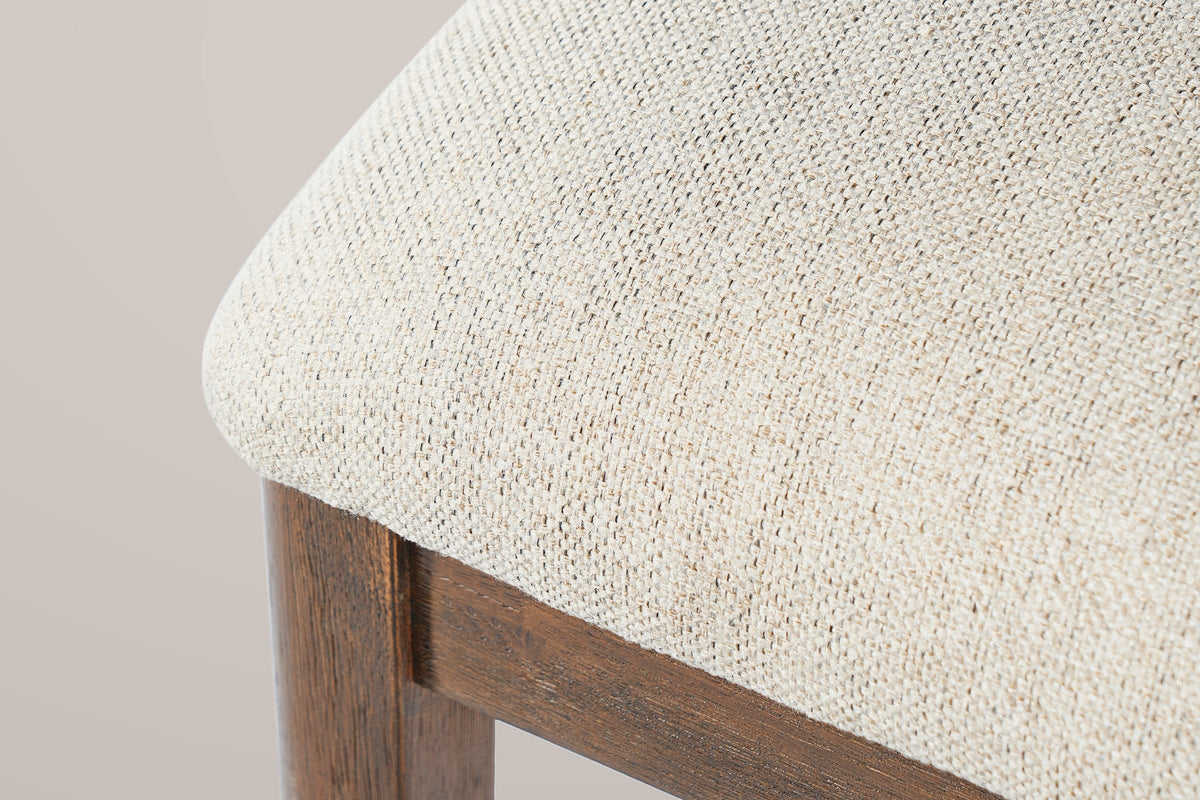 Close-up of the beige woven seat fabric, the wooden apron and a walnut-finished leg