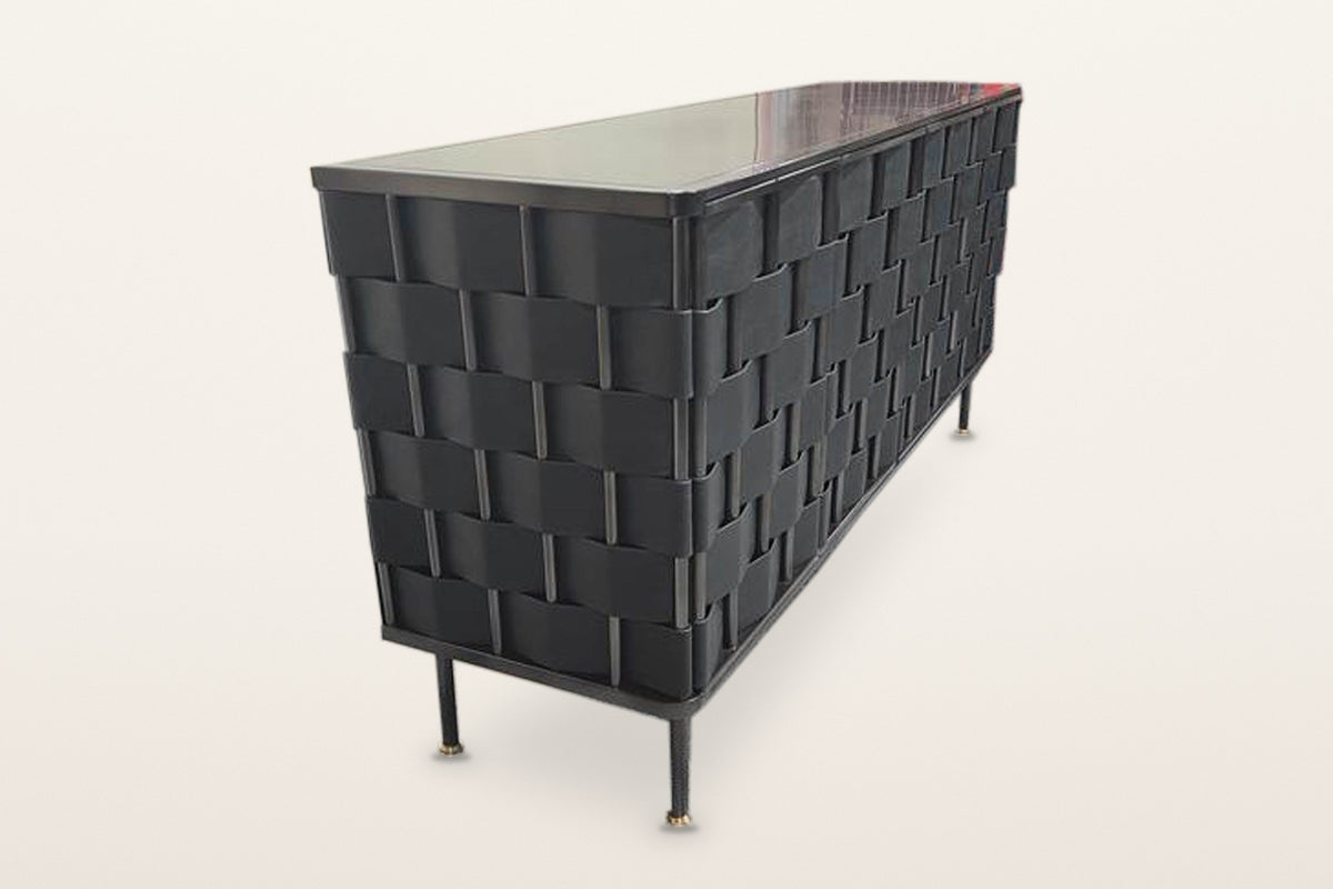 Trequanda woven leather sideboard in Black, raised three-quarter view from the end on a warm white studio backdrop: black lea