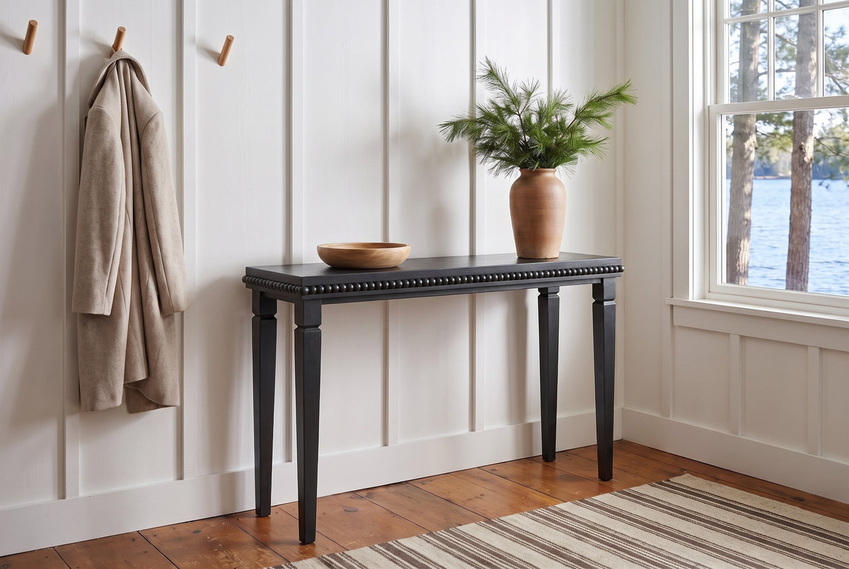 Treviso console table in Black in a white board-and-batten Muskoka cottage entry, pine branches in a clay vase