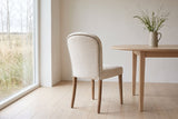Usseglio dining chair seen from behind, the row of antique-bronze nailheads round its cream back, beside a pale oak round table in a Saskatoon dining room