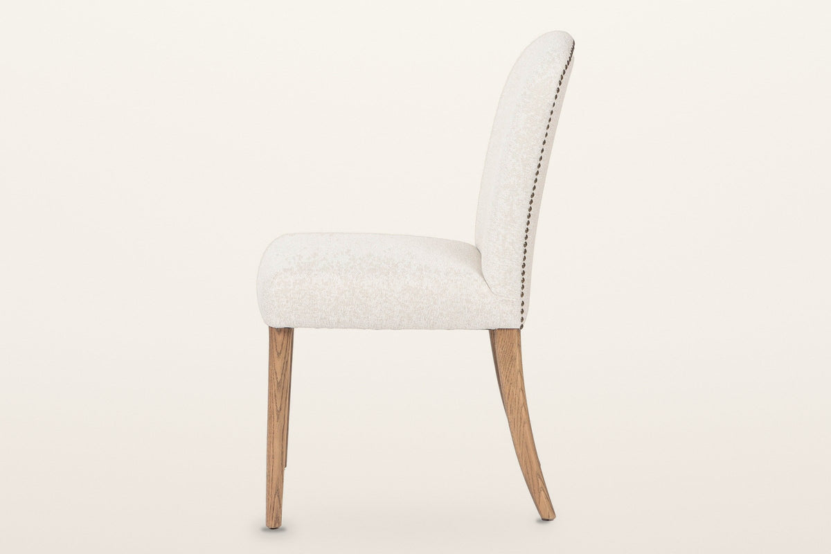Usseglio dining chair from the side: the back curving gently backward, the nailhead line along its rear edge and the swept-back rear legs